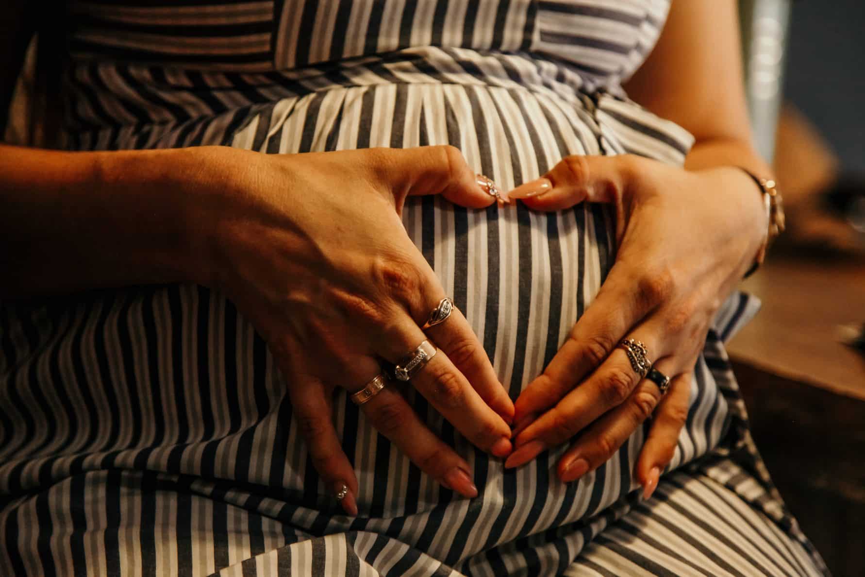 eine Schwangere hält ihre Hände zum Herz geformt auf dem Bauch